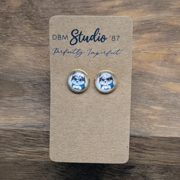 Small round glass cabochon earrings in gold tone. An image of a cartoon dog wearing glasses, with a blue scarf holding a coffee inside.
